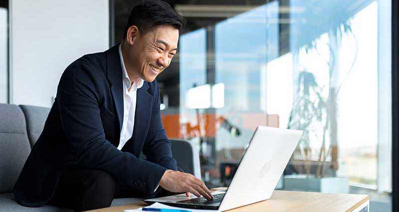 Senior Asian business man working on laptop online, smiling and rejoicing, happy boss business owner working in office