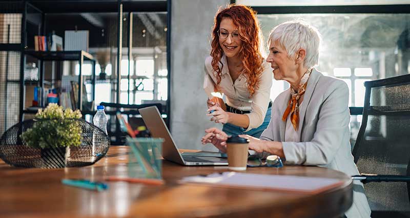 An old and young businesswomen smiling at laptop at the office.